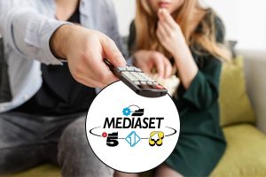 Persone sedute sul divano col telecomando e logo Mediaset in un riquadro