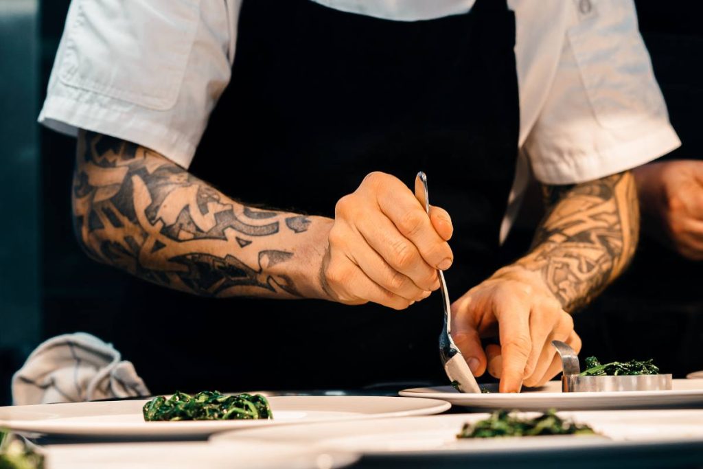 Chef tatuato che impiatta della verdura