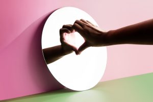 Donna che fa il simbolo del cuore con la mano allo specchio: simbologia di amare sé stessi