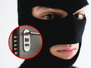 Ladro con un passamontagna, e in evidenza una serratura con maniglia