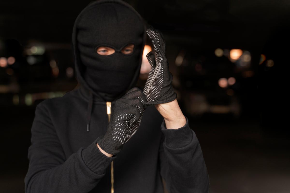 Un ladro con il volto coperto che si infila i guanti