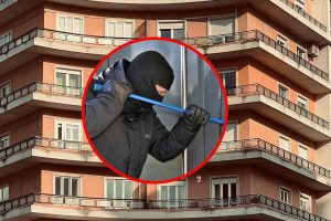 Un ladro che prova a scassinare una porta, in evidenza. E in secondo piano un palazzo