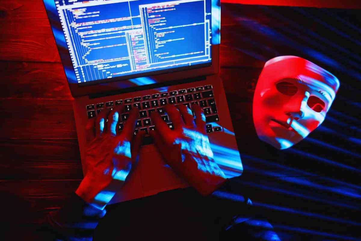 Uomo che digita un codice su laptop e maschera poggiata sulla scrivania