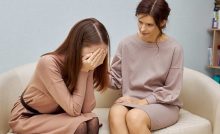donna seduta sul divano con le mani in faccia e accanto a lei un'altra donna