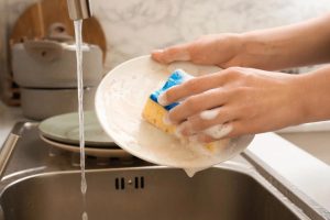 Persona che lava un piatto con detersivo e spugna
