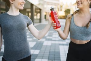 Ragazze che si passano una bottiglia di sport drink rosso