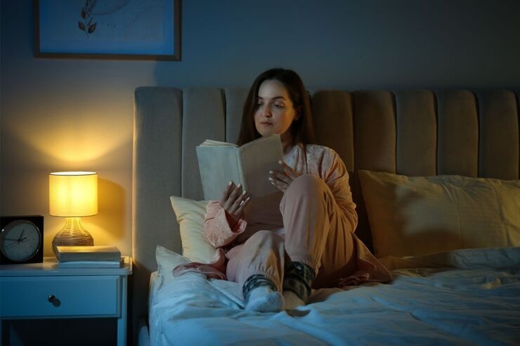 Donna legge un libro sul letto al buio con luce sul comodino accesa