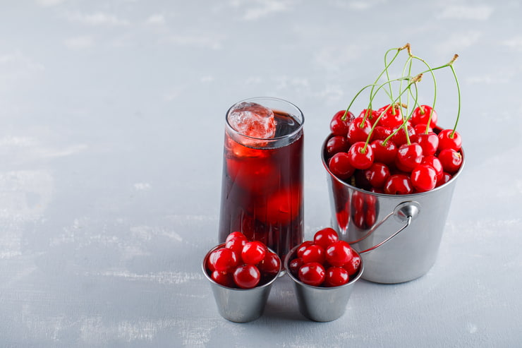 Bicchiere di succo rosso accanto a ciotole di ciliegie
