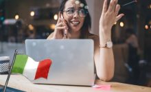 donna con pc davanti che parla a telefono e bandiera italiana
