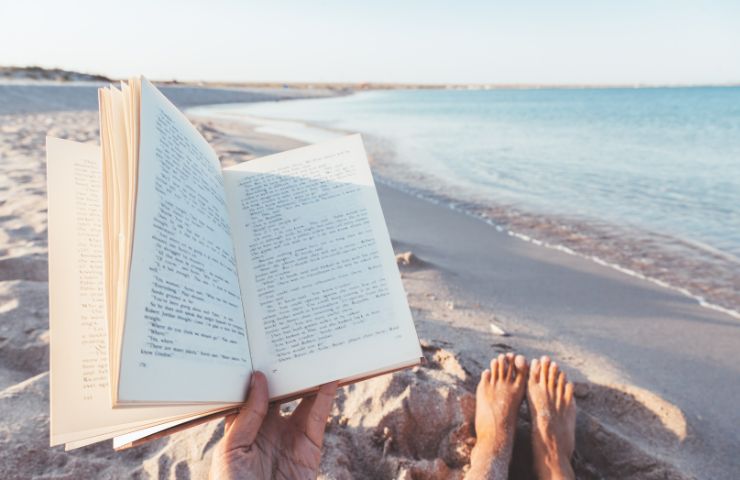 uomo che legge libro a riva di mare
