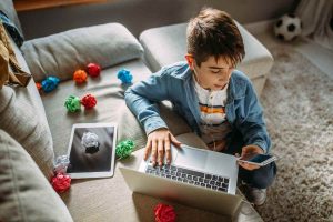 bambono con cellulare e cuffie pc tablet e disordine sul divano