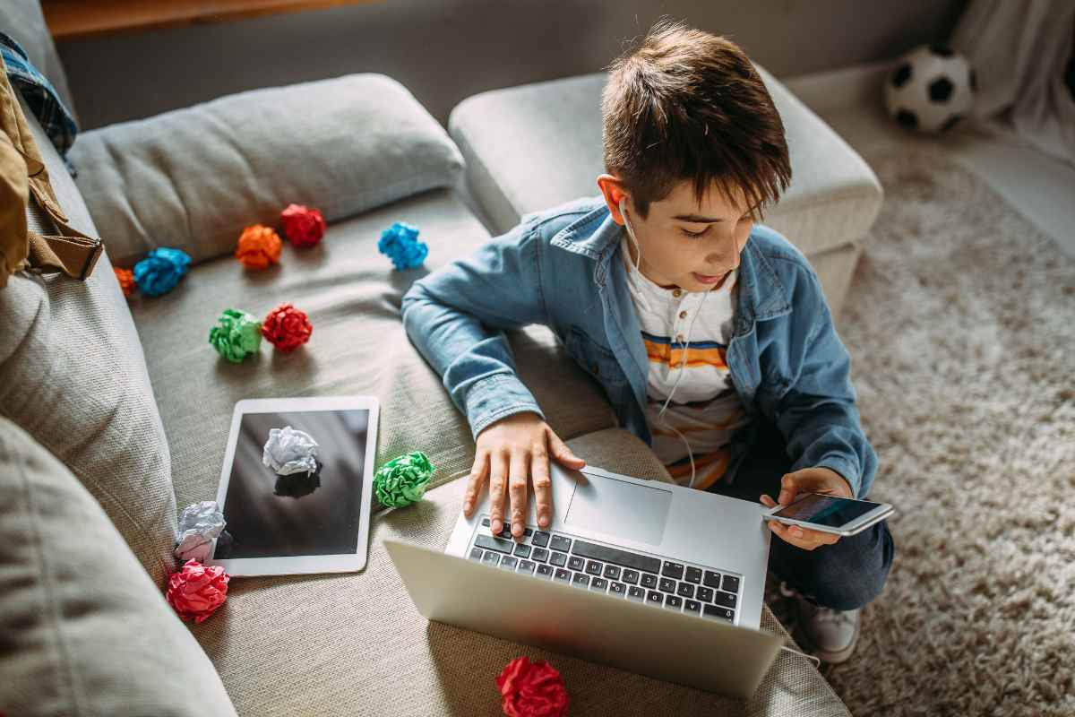 bambono con cellulare e cuffie pc tablet e disordine sul divano