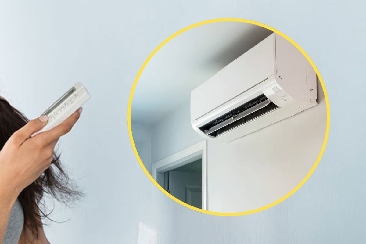 Una mano con un telecomando del condizionatore e in evidenza lo spit di un climatizzatore domestico